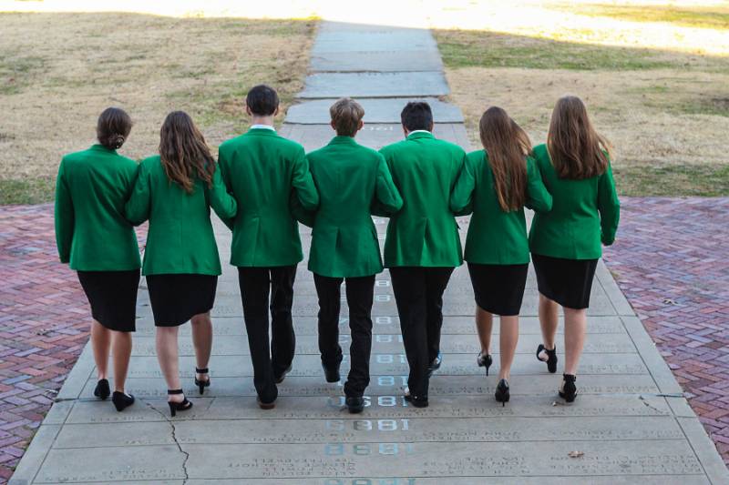 The 7 state officers in green suit jackets, walking away from the camera, linked arms.