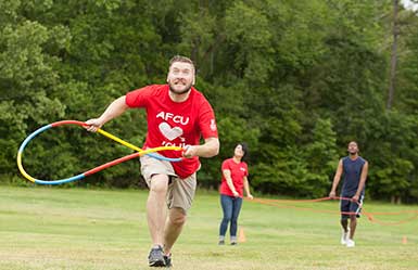 Man running with hoola-hoop in hand, other adults participating in teambuilding activties in background.