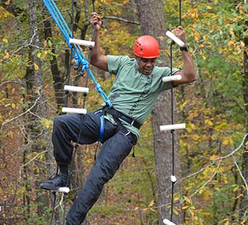 Adult male in harness and orange helmet on a high ropes course activity.
