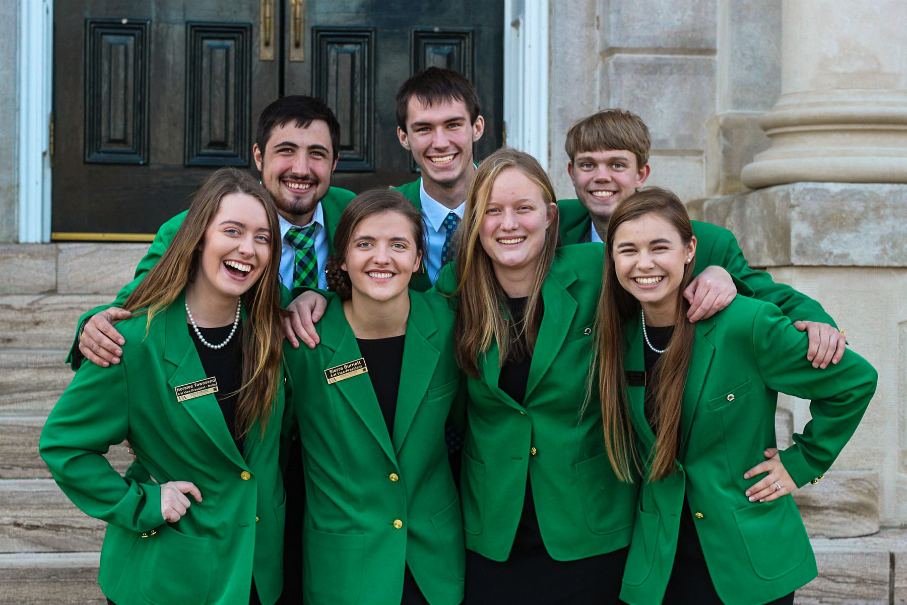 7 state officers, 4 girls in front and 3 boys in back, wearing kelly green blazers.