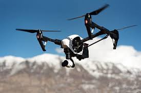 Image of a white drone with black propellers in air with snow covered moutains in background.