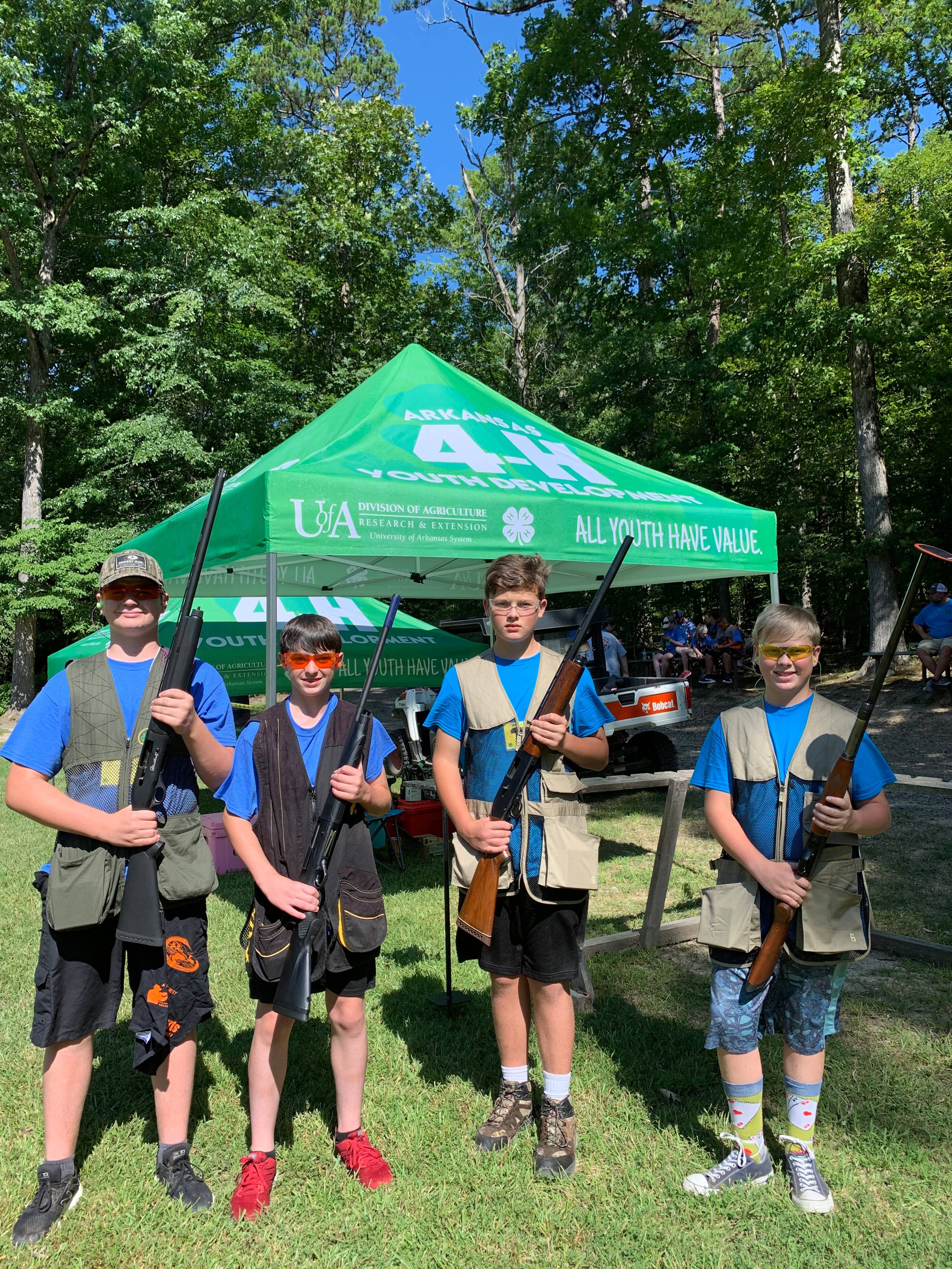 Male 4-H Youth outdoors, safely holding firearms before competing in shooting sports competition.