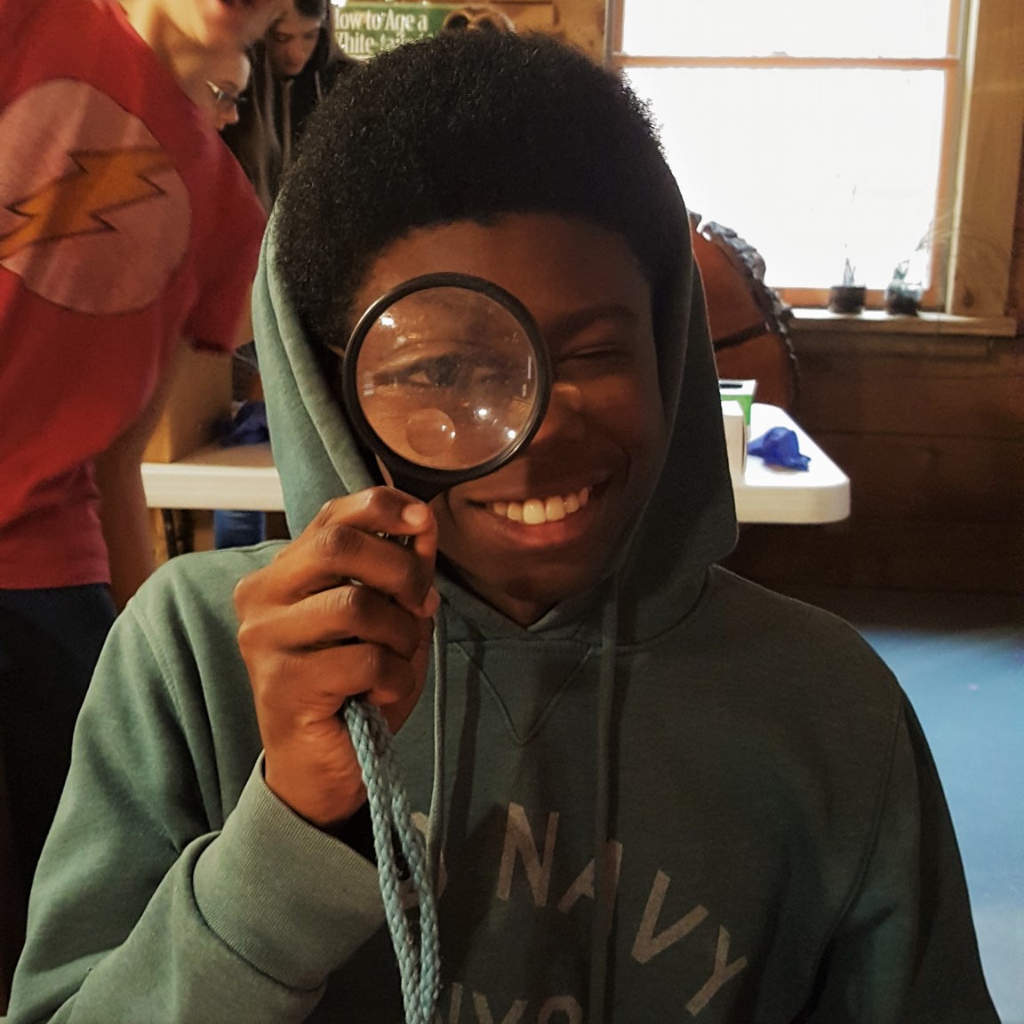 Young male student holding magnifying glass up to his eye.