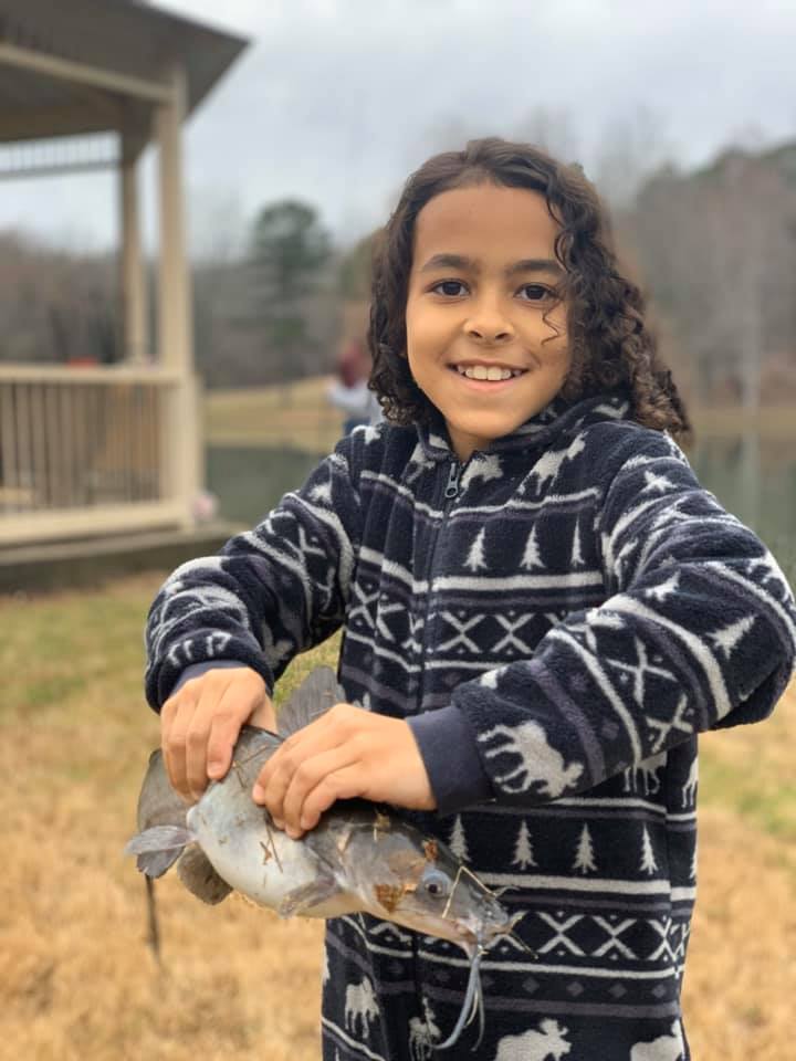 Young boy holding a catfish in both hands, lake in background.