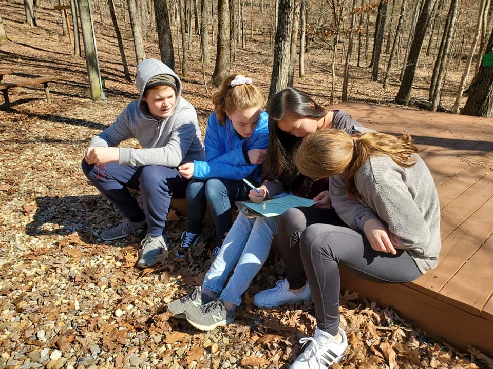 4 students outdoors, sitting on a deck working together on a worksheet