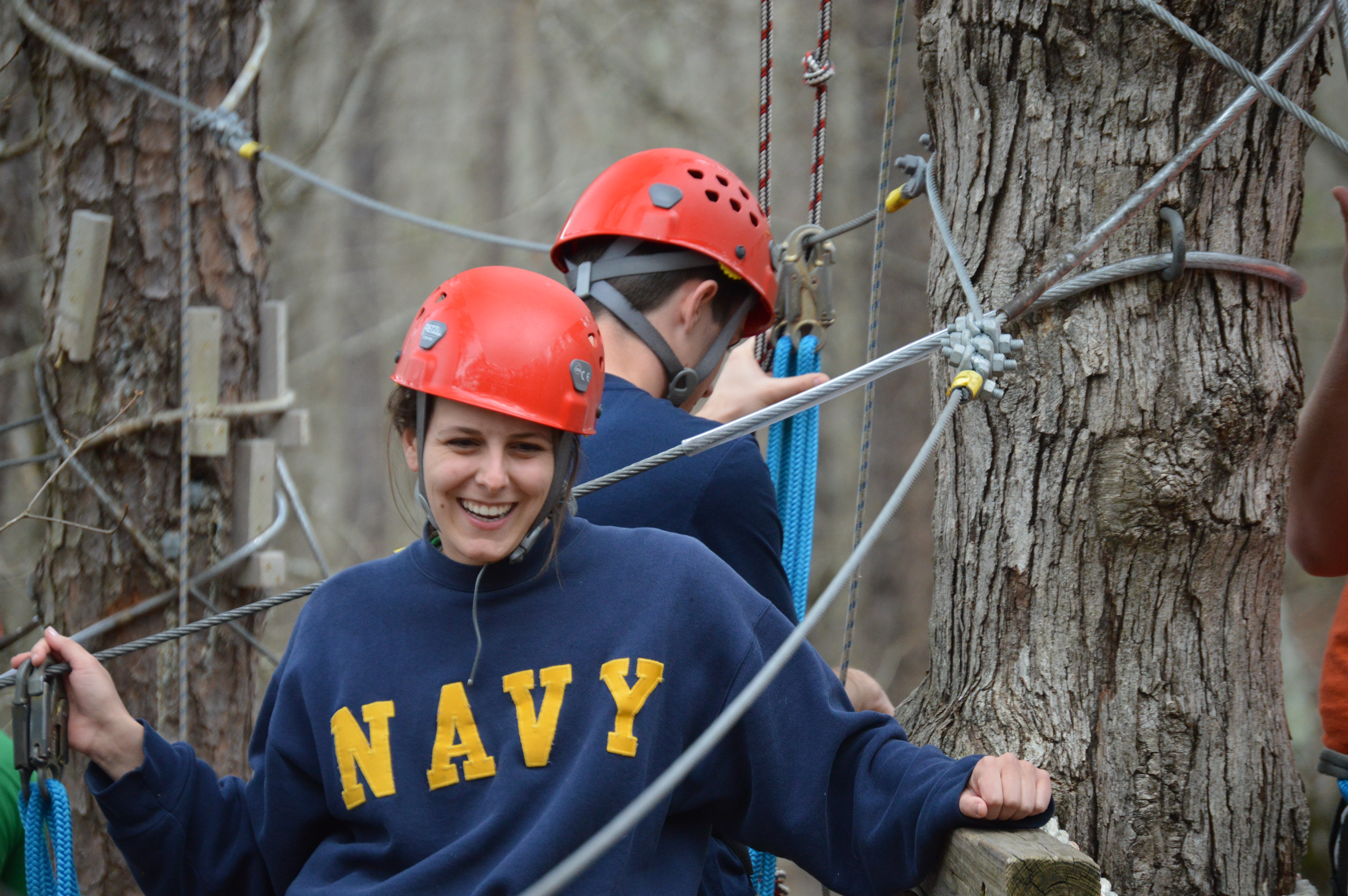 Young girl in orange helmet on the ropes course at the Arkansas 4-H Center, there is a tree on each side of her.
