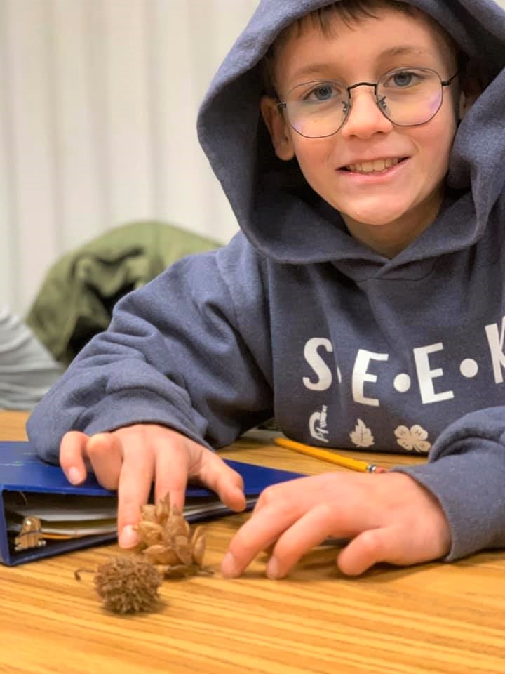 Male student in a SEEK hoodie with wildlife samples on the table in front of him.
