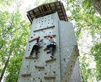 2 youth in orange helmets climbing a rock wall structure.