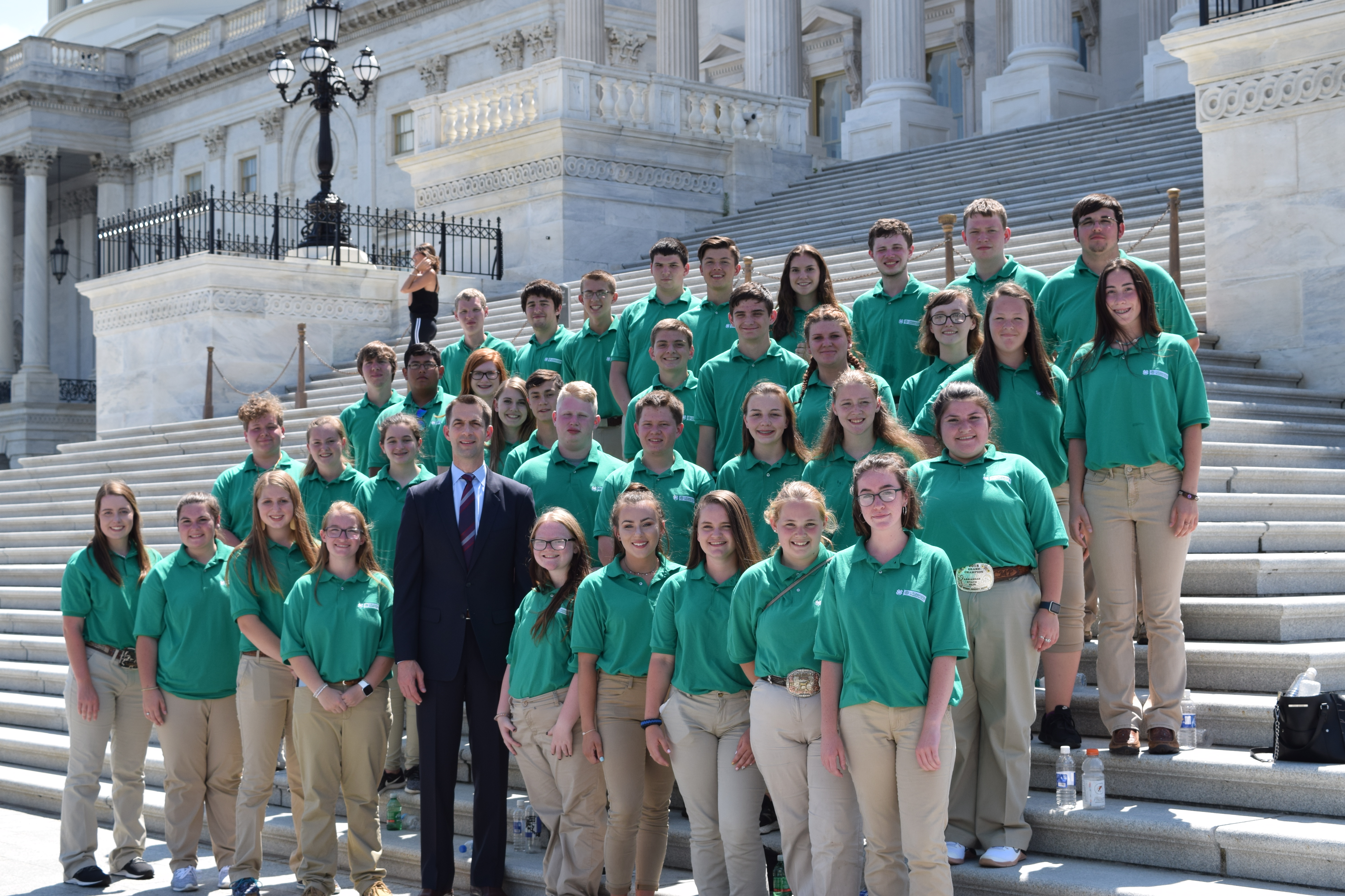 A large group of 4-H students wearing green polo shirts stand on the steps of the U S Capitol building with arkansas senator tom cotton 